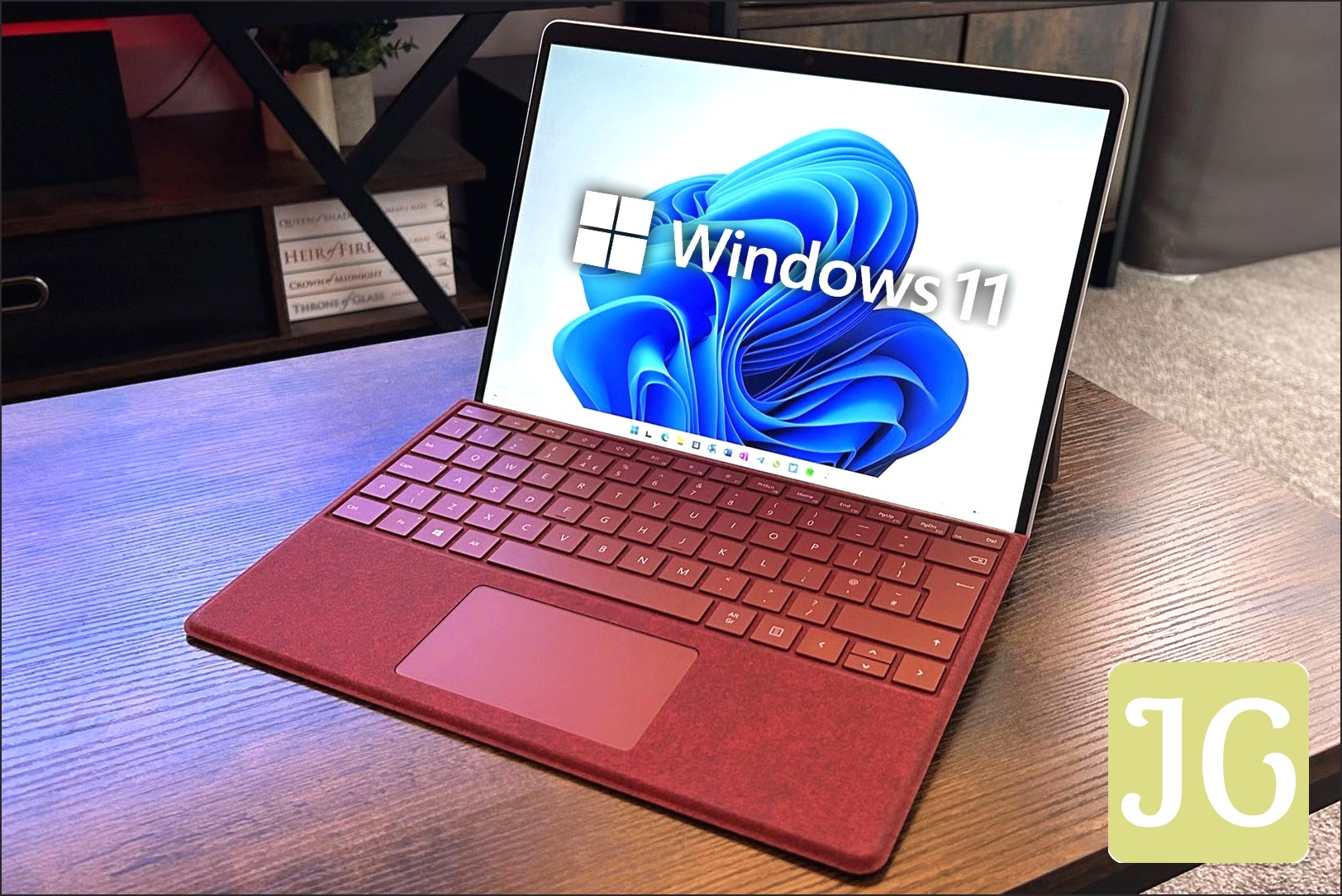 Windows 11 logo superimposed onto the screen of a Microsoft Surface Pro 9 with a red keyboard seated on a wooden desk, symbolizing the problematic update.