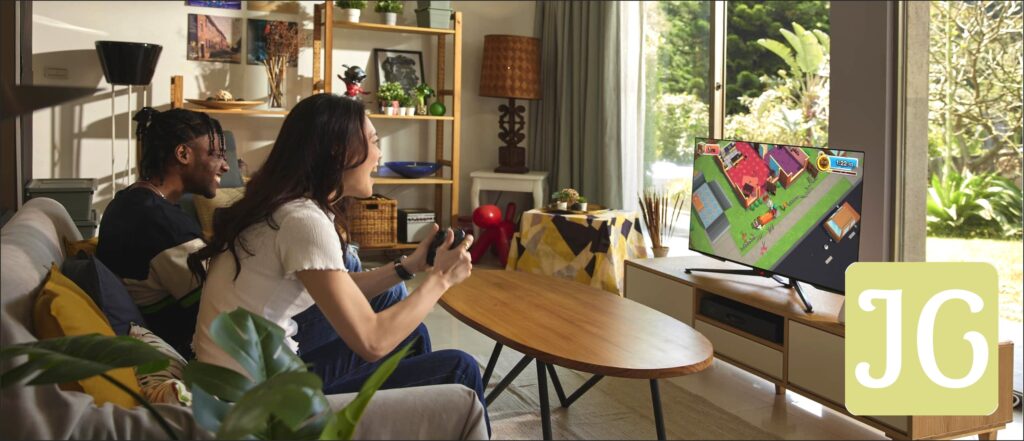 Two people sitting on a living room couch, with the Ally connected to a TV, playing a multiplayer game together.